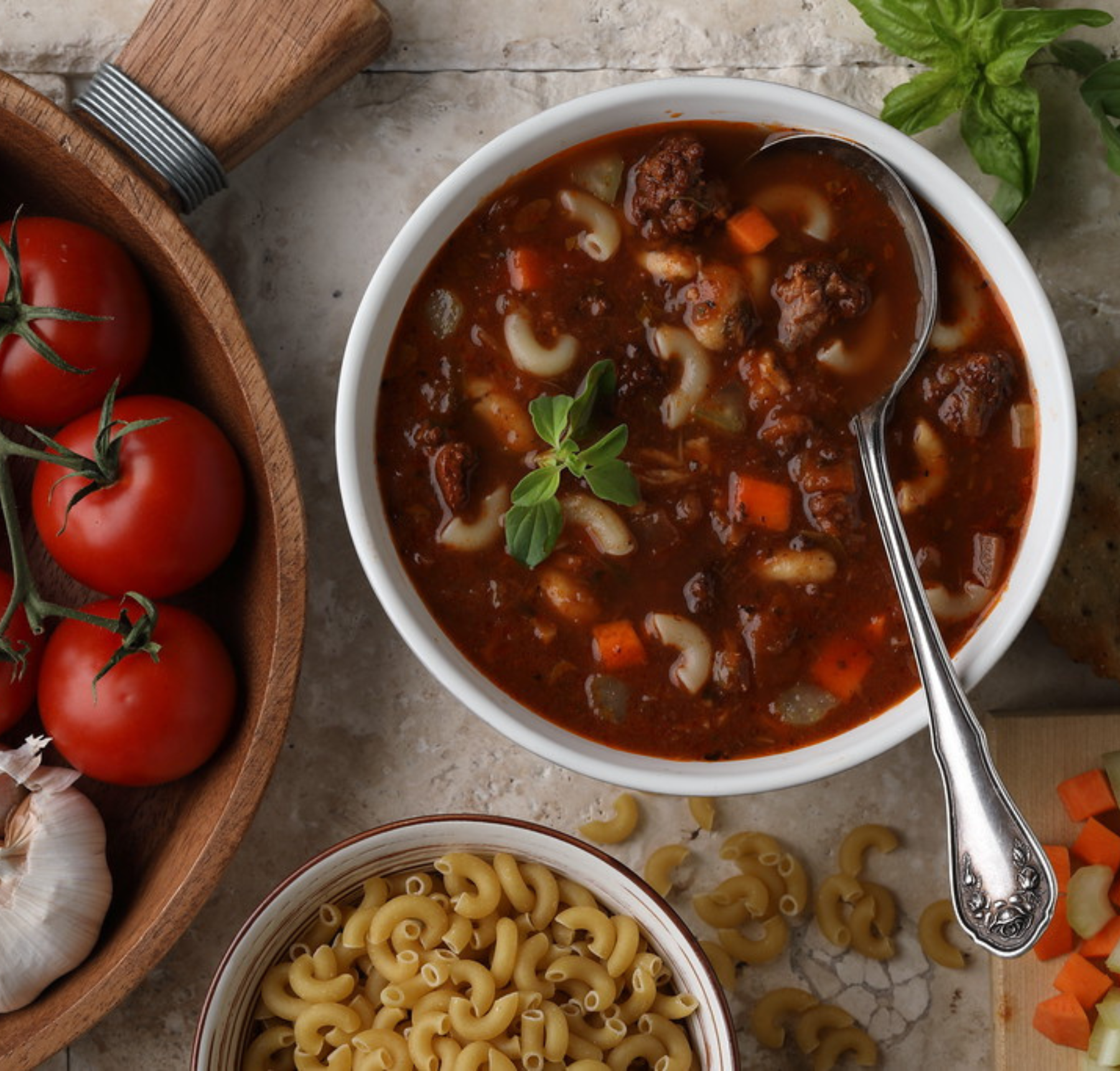 A bowl of hangover soup featuring ground beef, vegetables including onions, carrots, and celery, and elbow macaroni, garnished with a leaf of parsley.