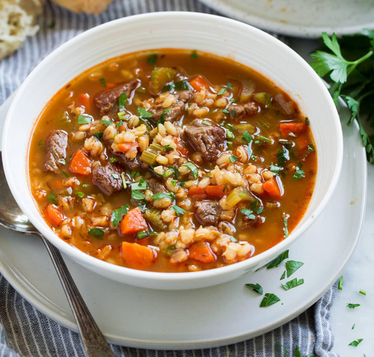 A bowl of hearty beef barley soup with visible ingredients including carrots, onions, and parsley.
