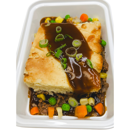 A serving of Shepherd's Pie in a white dish, with a golden-brown crust and gravy drizzled over the top along with green onions.