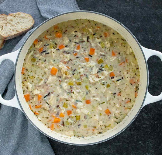 A pot of turkey wild rice chowder with visible chunks of turkey, wild rice, and vegetables like onions and carrots in a creamy broth.